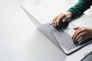 man working online on the white table at office, hands holding pen and typing on laptop keyboard